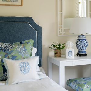 Monogrammed Linen boudoir pillow sham with a light blue hemstitch border. Displayed on a bed with blue headboard and GP & J / Lee Jofa Hydrangea Bird decorative pillow and bench, blue and white ginger jar lamp with scalloped lamp shade, chinoiserie chic mirror, white desk, monogrammed tissue box cover and rattan cane covered container filled with flowers.