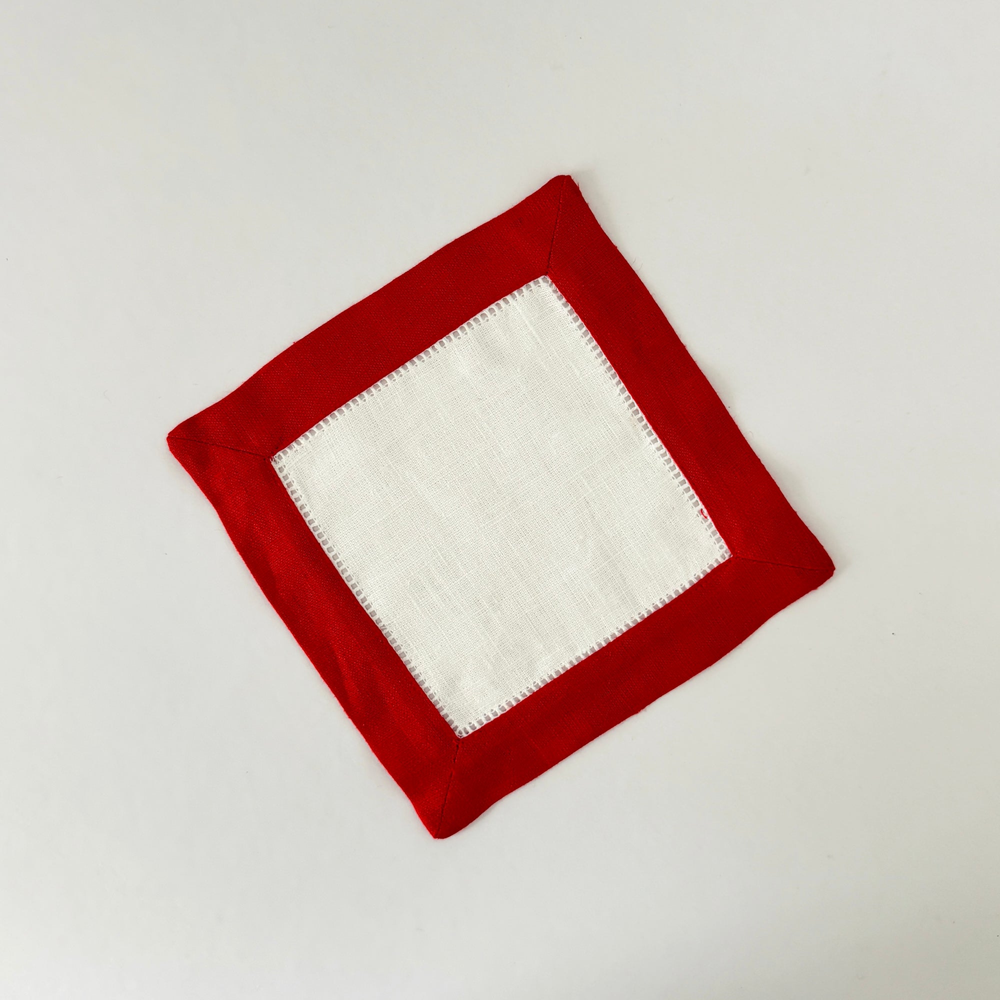 White linen cocktail napkin with a colored linen hemstitch border. Featured with border color Merry Red. Approximately 6.5" x 6.5" square.